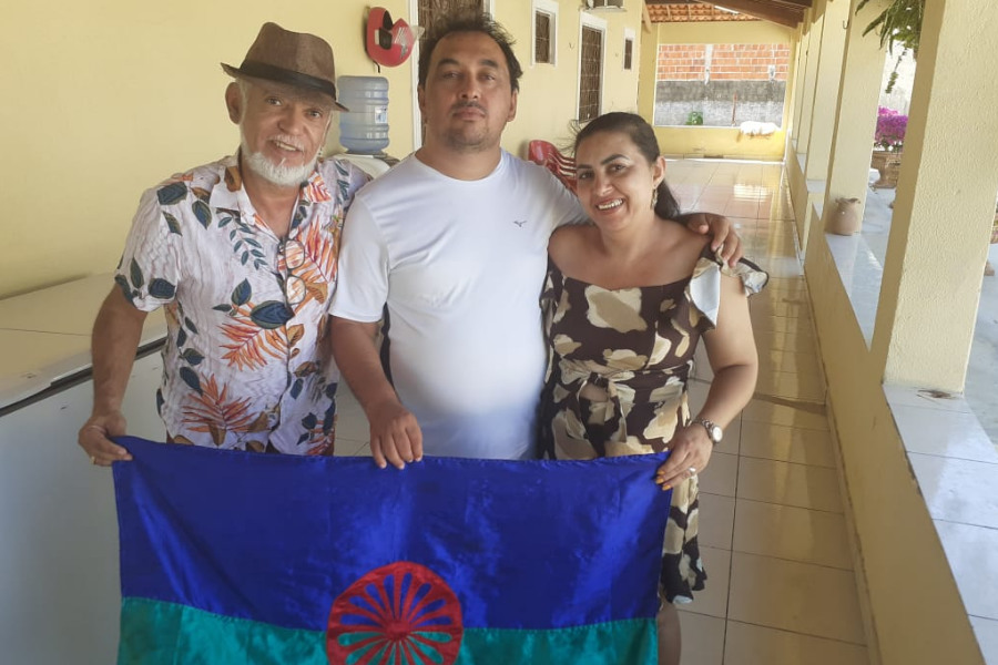 Rogério Ribeiro, José Pereira da Silva, o Nego Bom e sua esposa posam segurando a bandeira do Instituto Cigano do Brasil em uma varanda