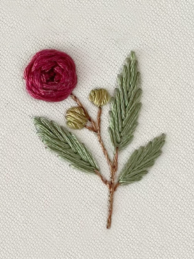 Uma rosa vermelha bordada em um tecido de algodão cru