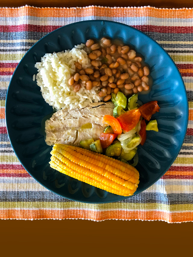 Prato de comida com arroz, feijão, milho, salada e peixe