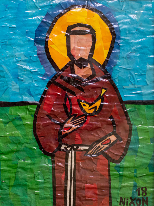 Imagem de São Francisco de Assis feita em mosaico de papel. São Francisco veste uma roupa marrom, e segura um passarinho amarelo. Ao fundo há um cenário azul e verde