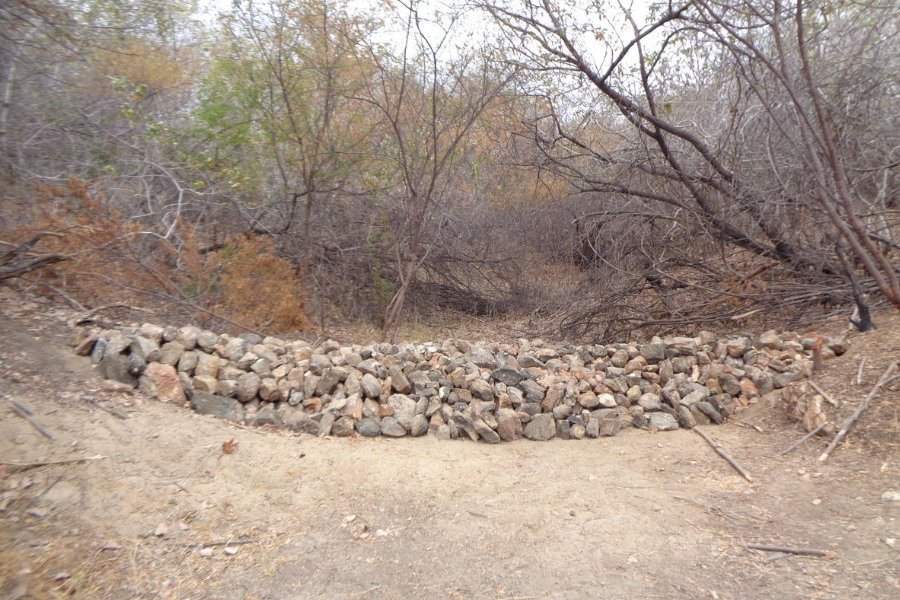 Barragem construída com pedras no leito de um riacho seco com vegetação seca ao redor