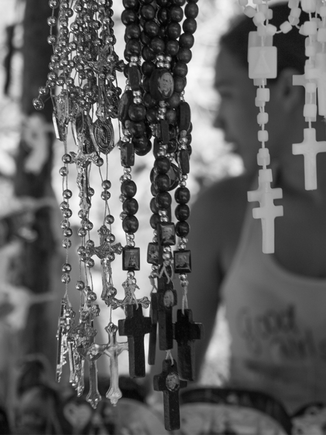 Fotografia em preto e branco de terços feitos em contas escuras e claras expostos à venda em uma banquinha de artesanato em Juazeiro do Norte