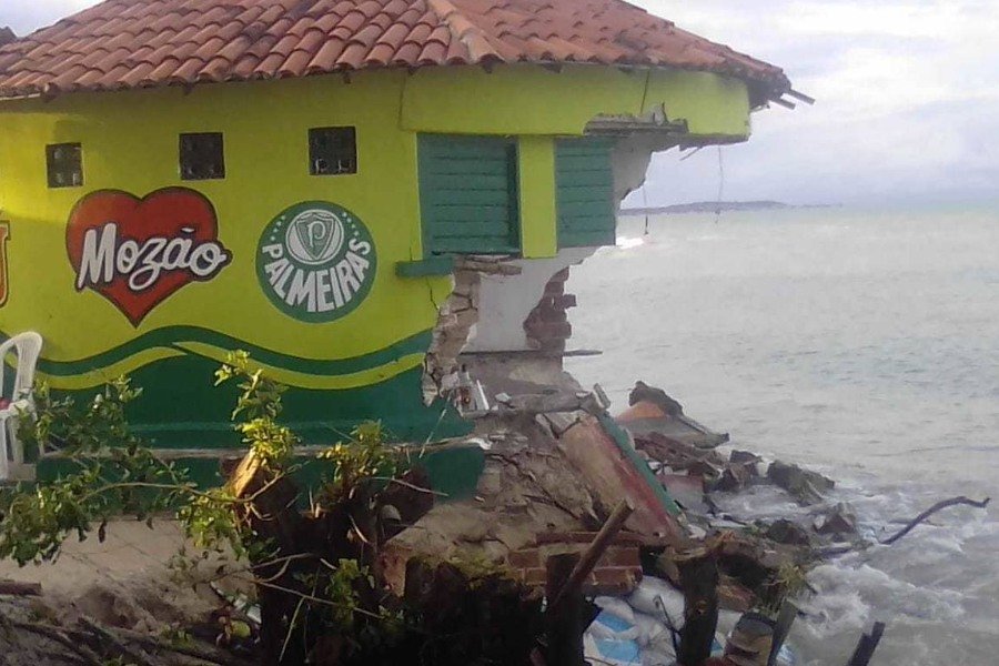 Bar amarelo com faixa verde, coração vermelho com Mozão escrito em letras brancas e escudo do Palmeiras com grande pedaço levado pela força do mar, à direita