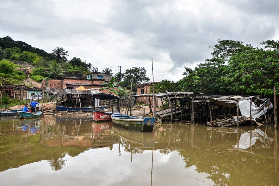 Foto de rio com água barrenta, embarcações coloridas, cobertas de telha e madeira e, ao fundo, casas simples, de tijolos aparentes