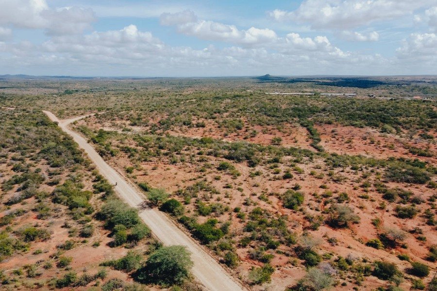 Foto aérea de área em avançado estado de desertificação com uma estrada cortando a paisagem de chão avermelhado com pequenos arbustos verdes