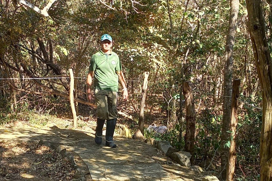 Fotografia de Homem usando trajes verdes e boné da mesma cor, caminhando em um caminho de cimento em meio a uma vegetação verde de Caatinga