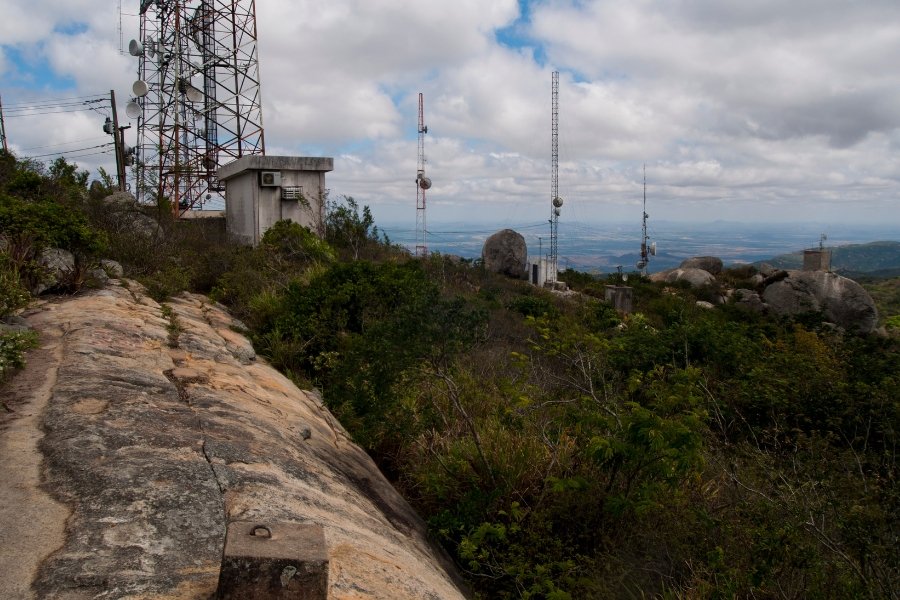Parte inferior da imagem: rocha com torre de telecomunicação à esquerda e ao fundo a vista de serra