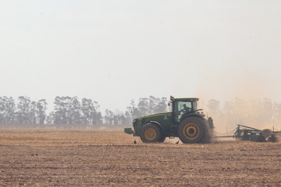 Fotografia colorida mostra trator puxando um arado. Ao volante aparece a silhueta de um homem. Atrás da plantação tem uma rala vegetação de Cerrado