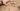 Foto colorida de pegadas de animal em areia marrom molhada com duas mãos de mulher branca espalmadas ao lado, destacando as marcas na areia. No pulso da mão esquerda há um relógio digital preto e no dedo médio da mão direita um anel preto