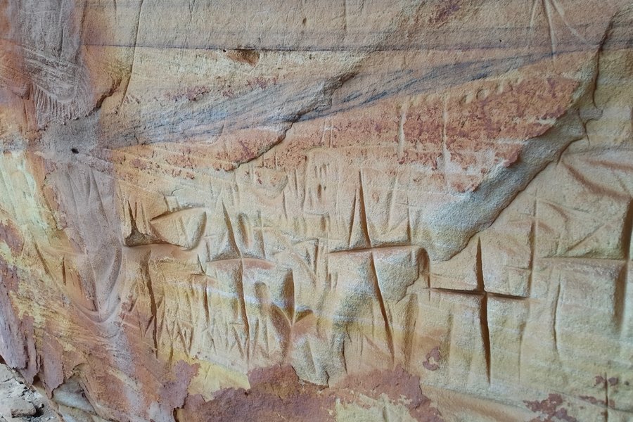 Fotografia de gravuras rupestres em uma superfície rochosa avermelhada. As imagens grafadas se assemelham a cruzes