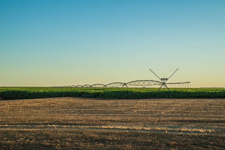 Foto colorida do campo com extensa estrutura de irrigação chamada de pivô central separando área plantada de soja e terreno sendo preparado para plantio 