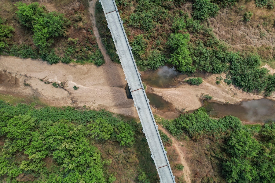 Foto aérea colorida de ponte sobre rio praticamente seco de fundo de areia clara ladeado por vegetação