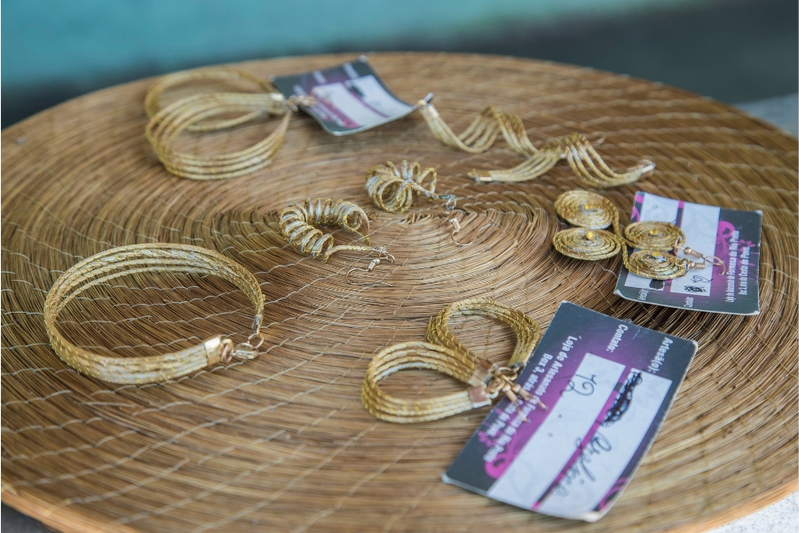 Foto colorida de brincos e pulseiras feitos de capim dourado dispostos sobre suporte para prato feito do mesmo material