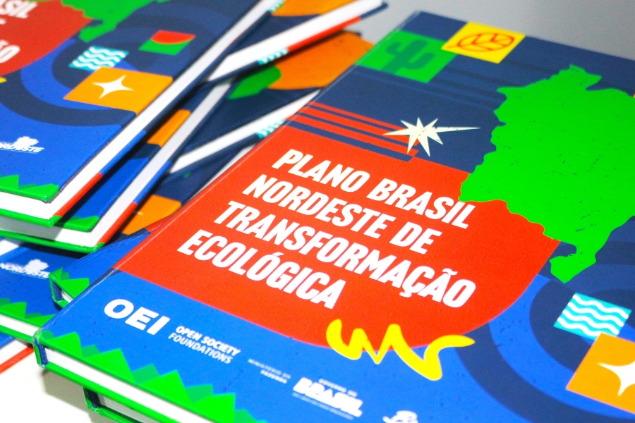 Foto de uma pilha de livros coloridos com capas vibrantes em tons de azul, vermelho, verde e amarelo. O título em destaque na capa diz “Plano Brasil Nordeste de Transformação Ecológica”. O design inclui formas geométricas, um mapa da região Nordeste em verde, ícones que remetem à natureza e à sustentabilidade, e os logotipos da OEI (Open Society Foundations) na parte inferior