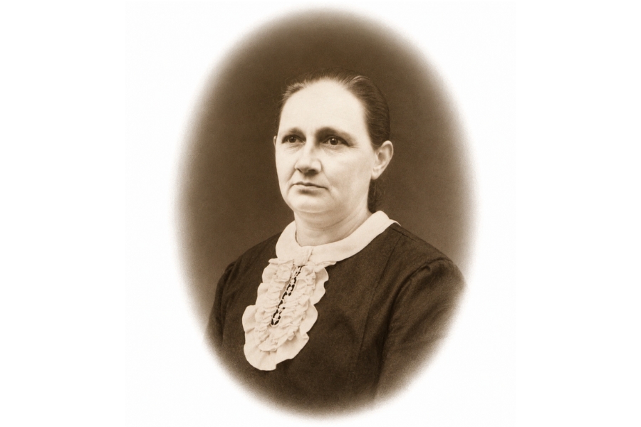 Retrato em tom sépia em moldura oval de uma mulher de vestido escuro com gola e babados claros no peito.