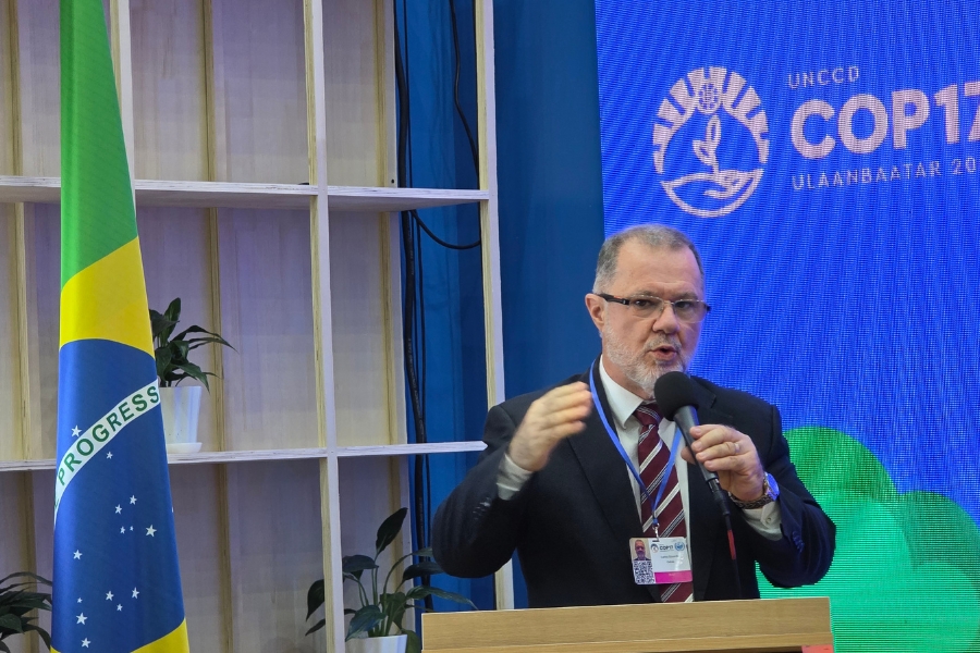 Homem de terno escuro, gravata listrada e óculos discursando em um púlpito com microfone na mão. Ao lado esquerdo está a bandeira do Brasil e, ao fundo, um painel azul da UNCCD COP17 (Ulaanbaatar).