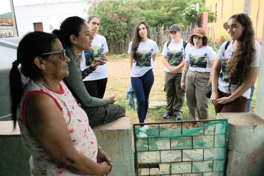 Grupo de voluntários/pesquisadores vestindo camisetas do projeto em conversa de conscientização ambiental na entrada da residência de uma moradora local.