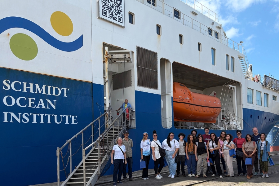 Equipe reunida no cais ao lado da imponente estrutura lateral do navio de pesquisa oceanográfica com a inscrição "Schmidt Ocean Institute".