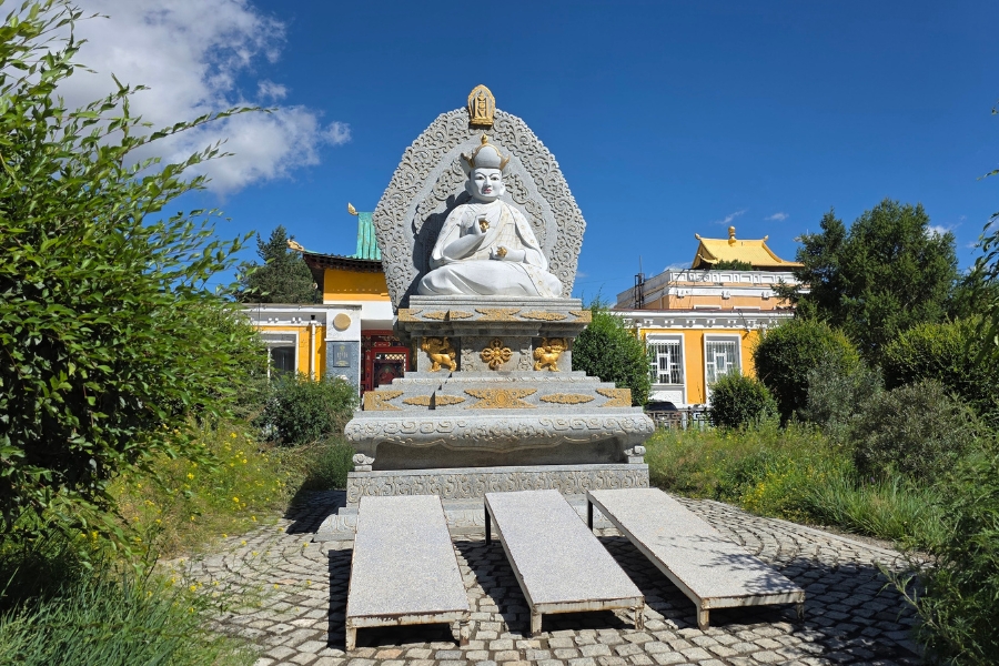 Estátua de uma divindade budista sentada em posição de meditação diante de um templo.