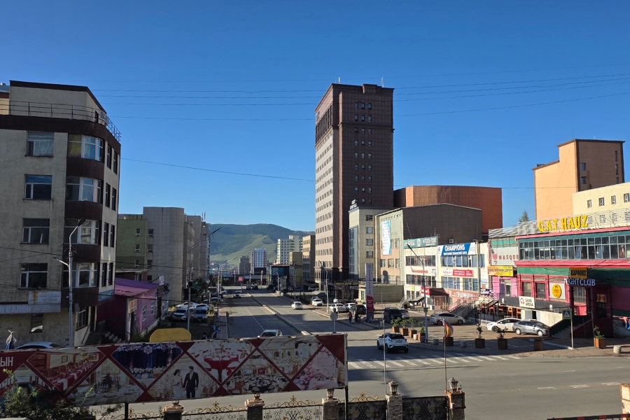 Vista urbana da cidade de Ulaanbaatar com ruas, prédios modernistas e montanhas ao fundo.