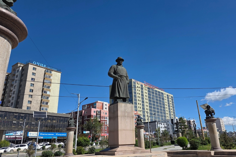 Estátua de bronze em uma praça pública com edifícios da cidade ao fundo.