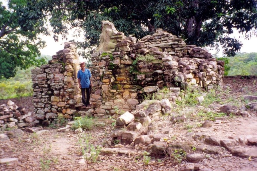 Homem em pé no portal de ruínas históricas construídas com pedras sobrepostas cercadas por vegetação